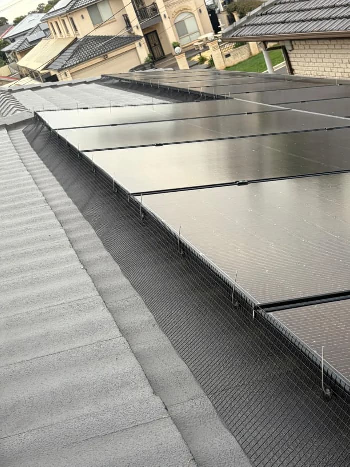 All-black solar panels with perimeter bird mesh installed along a concrete tile roof